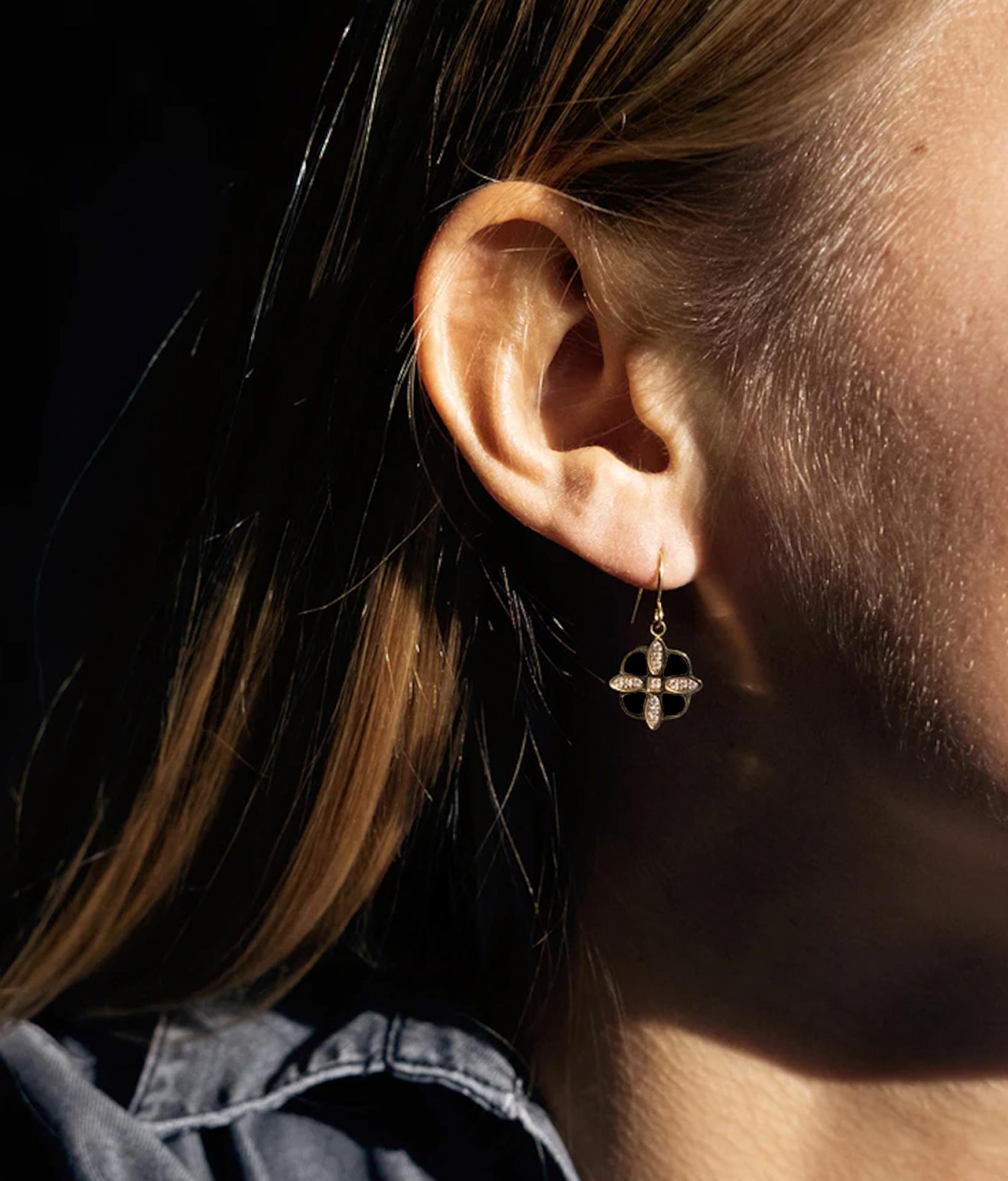 Junge Frau trägt elegante goldene Ohrringe in einer Blumen Form aus schwarzem Onyx Stein und Zirkonia